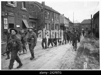 Britische Truppen marschieren deutsche Gefangene während ihrer ersten Schlacht auf deutschem Boden im Zweiten Weltkrieg durch ein erobertes Dorf in Deutschland Stockfoto