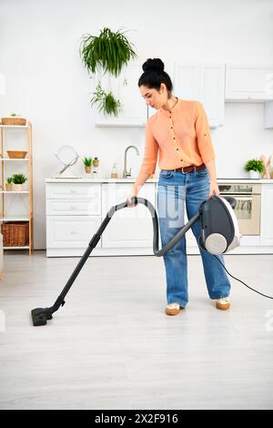 Eine stilvolle Frau in lässiger Kleidung saugt effizient ihren Küchenboden auf, um ihr Zuhause makellos zu halten. Stockfoto