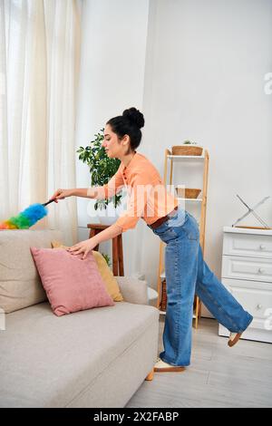 Eine stilvolle Frau in lässiger Kleidung reinigt sorgfältig eine Couch mit einem Mopp und verschönert ihren Wohnraum. Stockfoto