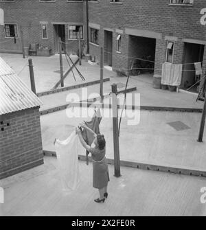 THE COTTAGES OF FREEFOLK: LIFE IN THE VILLAGE OF FREEFOLK, HAMPSHIRE, ENGLAND, 1943 - Eine Frau hängt ihre Wäsche im Hinterhof ihres Cottages in Freefolk, Hampshire. Jedes Häuschen hat einen Gemüse- und Blumengarten an der Vorderseite des Hauses, aber ein Betonhof an der Rückseite der Häuser, komplett mit permanenten Kleiderpfosten Stockfoto