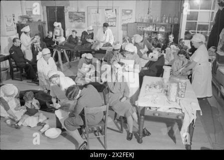 DER WIEDERAUFBAU EINES "VORFALLS": ZIVILSCHUTZAUSBILDUNG IN FULHAM, LONDON, 1942 - Eine geschäftige Szene im Behandlungsraum der First Aid Post, eingerichtet in einem Raum in einer Schule, wahrscheinlich Mary Boon School, an der Ecke Earsby Street und Bishop King's Road, in der Nähe der Avonmore Road. Krankenschwestern behandeln verschiedene Verletzungen, einschließlich des verletzten Beins eines Jungen. Im Hintergrund kümmern sich der Arzt und die Pflegekraft um einen Mann mit einer Rückenverletzung. An der Wand sind zahlreiche Plakate zu sehen, die die Menschen ermutigen, die Kriegsanstrengungen auf verschiedene Weise zu unterstützen Stockfoto