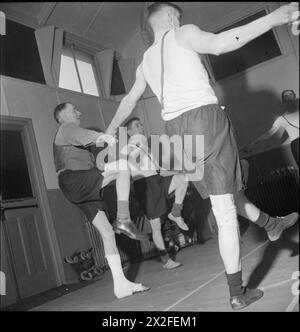 FABRIKWOHLFAHRT: WOHLFAHRT IN PILKINGTON'S GLASFABRIK, ST HELENS, LANCASHIRE, ENGLAND, VEREINIGTES KÖNIGREICH 1944 – Männer mit Bein- und Rückenverletzungen führen im Turnsaal des Rehabilitationszentrums der Fabrik (wahrscheinlich in der Glasfabrik Pilkington in St. Helens) im Rahmen ihres Erholungsprogramms Gleichgewichtsübungen durch. Die Männer stehen im Kreis und halten die Hände, während sie ihre Beine in der Luft hochheben. Der Originalüberschrift zufolge ist es das Ziel [des Zentrums], Männer und Frauen daran zu hindern, dauerhaft behindert zu werden. Durch Übungen und Massagen unter der Leitung eines im Modus ausgebildeten Physiotherapeuten Stockfoto