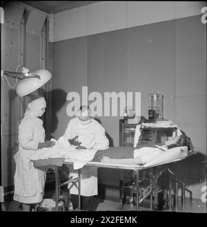 FABRIKWOHLFAHRT: WOHLFAHRT IN PILKINGTON'S GLASFABRIK, ST HELENS, LANCASHIRE, ENGLAND, VEREINIGTES KÖNIGREICH 1944: der Sheet Works Surgeon operiert am Bein einer Kriegshelferin im Operationssaal der Sheet Works Surgery, wahrscheinlich in der Pilkington Glass Works Works Works Works in St Helens. Die Sheet Works Chirurgie schließt sich dem Hauptgebäude an und Mitarbeiter können sich jederzeit von einem Arzt oder einer Krankenschwester behandeln lassen Stockfoto