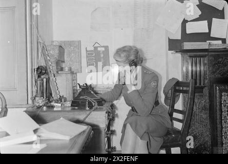 FLUGBOMBE: V1-BOMBENSCHADEN IN LONDON, ENGLAND, Großbritannien, 1944 - Eine Frau des amerikanischen Krankenwagens Großbritannien erhält einen Anruf, um ihre Teilnahme an einem Vorfall zu fordern Stockfoto