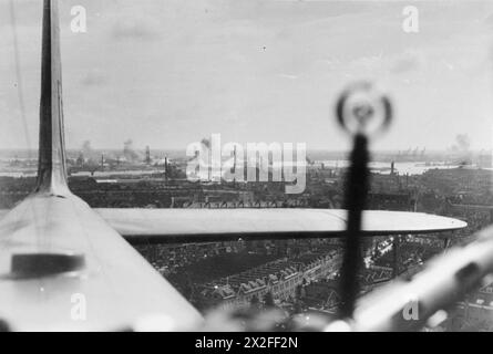 Ein schräges Luftbild, das während eines großen Tageslichtangriffs auf den Docks in Rotterdam, Holland, von Bristol Blenheim Mark IV von No. 2 Group aufgenommen wurde. Das Bild zeigt Bomben, die auf dem Dock platzen, während ein Blenheim-Flugzeug über die Dächer fährt, mit dem Heck des Flugzeugs links und dem Schuss und einem Teil des Geschützes rechts im mittleren oberen Turm. Stockfoto