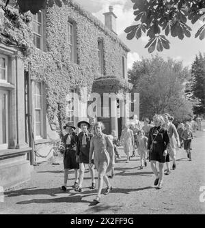 STADTVERWALTUNG IN Einer LANDSTADT: ALLTAG IN WOTTON-UNDER-EDGE, GLOUCESTERSHIRE, ENGLAND, Großbritannien, 1944 - Eine Gruppe von Kindern, hauptsächlich Mädchen, darunter mehrere in Girl Guide Uniform, spazieren im Sonnenschein vorbei an „Dryleaze“, einem Kinderheim, das vom Gloucestershire County Council in Wotton-under-Edge betrieben wird. Der ursprüngliche Titel besagt, dass es vom Ausschuss für öffentliche Unterstützung des Rates „auf „heimeligen“ Zeilen geführt wird und dass „seine Kinder an allen normalen Aktivitäten des normalen Stadtlebens teilnehmen und trainiert werden, ihren Lebensunterhalt zu verdienen, wenn sie die Schule verlassen. Die Mädchen bleiben länger dran als die bo Stockfoto