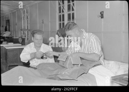 REHABILITATION BRITISCHER SOLDATEN AUS DER NORMANDIE: DIE ARBEIT DES ROBERT JONES AND DAME AGNES JAGDKRANKENHAUSES, OSWESTRY, SHROPSHIRE, ENGLAND, VEREINIGTES KÖNIGREICH, 1944: Corporal M Barnes (rechts) raucht eine Zigarette, während er sich in seinem Krankenhausbett aufsetzt, um ein neu angekommenes Paket im Robert Jones and Dame Agnes Hunt Orthopaedic Hospital in Oswestry zu öffnen. Corporal Barnes stammt aus Burnley in Lancashire und diente bei den Royal Welch Fusiliers. Er teilt den Inhalt seines Pakets mit seinem Kollegen Private Rennison (aus Bramley, Yorkshire), der bei der 51. Highland Division British Army, R, diente Stockfoto