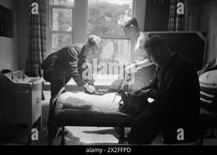 AMERIKANER IN GROSSBRITANNIEN: ANKUNFT DES ZIVILEN TECHNISCHEN KORPS, BOURNEMOUTH, ENGLAND, 1941 - neue Rekruten des zivilen technischen Korps (CTC) kleiden sich im Zimmer ihres Billet, wahrscheinlich im Annerley Court Hotel, Bournemouth. Von links nach rechts sind sie: Henning (Champaign, Illinois), der seine Schnürsenkel bindet, B Shapiro (Chicago), der seine Hose anzieht, und Gates (Brooklyn, New York), der in seine Tasche schaut Stockfoto