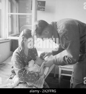 DIE BEFREIUNG DES KONZENTRATIONSLAGERS BERGEN-BELSEN, JUNI 1945 – Vater Vincent Fay, Kaplan der britischen Armee des 9. Britischen General Hospital, tauft ein Baby, Henji Dorochova, der in Belsen geboren wurde. Das Baby wird von seiner Mutter Raissa aus Woroshilovgrad in der Ukraine gehalten. Während der britischen Hilfsaktion wurden die neuen Mütter gefragt, ob sie ihre Babys taufen wollen und wenn ja, unter welcher religiösen Konfession British Army, Royal Army Chaplains' Department Stockfoto