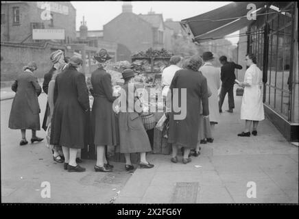 GROSSBRITANNIEN WARTET AUF ESSEN: RATIONIERUNG UND LEBENSMITTELKNAPPHEIT IN KRIEGSZEITEN, LONDON, ENGLAND, UK, 1945 - Housewives stehen an einem Gemüsestand an der Wood Green High Road. Der ursprüngliche Titel besagt, dass Kartoffeln, die einst als Grundpfeiler einer Mahlzeit galten, heute als seltene Preise angesehen werden und es Wert sind, darauf zu warten. Stockfoto