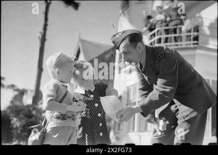 AMERIKANER IN GROSSBRITANNIEN: DIE ANKUNFT DES ZIVILEN TECHNISCHEN KORPS, BOURNEMOUTH, ENGLAND, 1941 - J E Beardwood vom zivilen technischen Korps bietet einem Jungen und Mädchen Süßigkeiten an, die auf einer sonnigen Straße in Bournemouth liegen. Beardwood stammt ursprünglich aus Brooklyn, New York und hat eine Frau und zwei Töchter in den Vereinigten Staaten Stockfoto