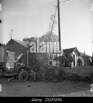 DIE NAAFI-KANTINEN SIND FÜR US-TRUPPEN bestimmt: DIE ARBEIT DER NAVY, DER ARMEE UND DER LUFTWAFFE, ENGLAND, Großbritannien, 1943 – zwei amerikanische Soldaten gehen in Richtung der NAAFI, irgendwo in England. Sie sind Corporal Mike Petrizzo (468 Villa Avenue, Port Richmond, Staten Island, New York) und Sergeant Joseph E Pavliscak (1743 Atchison Avenue, Whiting, Indiana). Im Vordergrund arbeitet PFC Thomas Healey (von 1 River Street, Proctor, Vermont) an seinem Lkw. Stockfoto