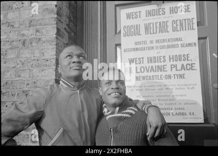 Zwei West Indian Merchant Seamen stehen 1941 vor dem West Indies House Hostel am 14-16 Lovaine Place in Newcastle-upon-Tyne. Ein Poster zeigt den Standort, die Einrichtungen und den Superintendenten Mr. Larbi. Stockfoto