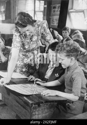 Ein DORF SPART: NATIONALE ERSPARNISSE IN LEWKNOR, OXFORDSHIRE, ENGLAND, 1941 - Mrs Scott hilft zwei Schülern der Dorfschule in Lewknor mit den Plakaten, die sie für einen Wettbewerb zeichnen, der vom National Savings Committee organisiert wird. Die besten dieser Plakate werden nach London geschickt, um im Rahmen des Wettbewerbs bewertet zu werden Stockfoto