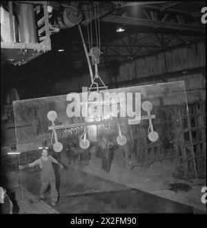 FABRIKWOHLFAHRT: WOHLFAHRT IN PILKINGTON'S GLASFABRIK, ST HELENS, LANCASHIRE, ENGLAND, VEREINIGTES KÖNIGREICH 1944: Arbeiten in einer Glasfabrik, wahrscheinlich in der Pilkington Glasfabrik in St. Helens. Eine große Glasplatte wird von einem Kran bewegt, aber von Hand von einem Arbeiter am Boden geführt. Dieses Stück Glas wird nach dem Gießen auf die Schleifmaschine übertragen, die das Glas schleift und poliert Stockfoto