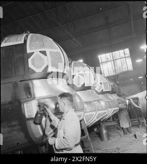 GEBURT Eines BOMBERS: FLUGZEUGPRODUKTION IN GROSSBRITANNIEN, 1942 - Lackierer in der Lackiererei der Handley Page Fabrik in Cricklewood. Papier wurde über die Fenster des vorderen Turms, des Cockpits und des Ablagefachs des Bombenflugzeugs dieses Halifax geklebt, um das Glas vor der Farbe zu schützen Stockfoto