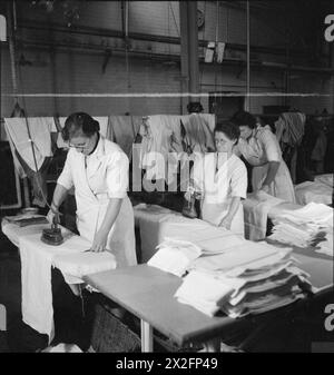 WÄSCHEREI IN KRIEGSZEITEN: DIE ARBEIT VON GLENIFFER WÄSCHEREI, CATFORD, LONDON, ENGLAND, UK, 1944: drei Arbeiter bei der Gleniffer Laundry in Catford Eisenbekleidung in der Handbearbeitungsabteilung. Einige Kleidungsstücke sind nicht zum Waschen und Bügeln in der Maschine geeignet und müssen daher von Hand gewaschen und gebügelt werden Stockfoto