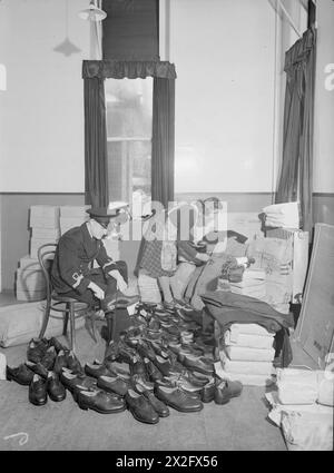 IN EINEM ADMIRALITÄT-BEKLEIDUNGSDEPOT. 17. OKTOBER 1944, MARINELAGER IM SÜDLICHEN GEBIET, GUILDFORD. OFFIZIERE, MÄNNER UND FRAUEN DER ROYAL NAVY WISSEN, DASS SIE EIN GUTES PREIS-LEISTUNGS-VERHÄLTNIS BEKOMMEN, WENN SIE IN DEN „PUSSERS STORES“ EINKAUFEN, DEM SPITZNAMEN DER NAVY FÜR DAS BEKLEIDUNGSDEPOT AN LAND ODER AUF SEE. JEDES KLEIDUNGSSTÜCK MUSS EINEN DOPPELTEN TEST BESTEHEN UND AUF QUALITÄT, GEWICHT UND DESIGNGENAUIGKEIT PRÜFEN, BEVOR ES DEN EIGENTLICHEN AUSSTELLUNGSRAUM FÜR KLEIDUNG ERREICHT. - Ein Marineoffizier wählt sich ein Paar Schuhe von den vielen vor ihm aus, während eine Assistentin die Adressen auf Kleiderballen aufträgt Stockfoto