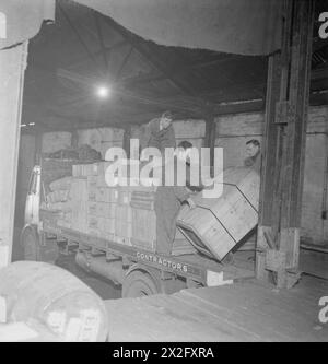 SIE FAHREN BEI NACHT: DIE ARBEIT DES LANGSTRECKENFAHRERS IN DER KRIEGSZEIT, ENGLAND, Großbritannien, 1944 – während der Lkw-Fahrer Fred Horrod in seinen Unterkünften schläft, laden Arbeiter im Depot von H & G Dutfield in Manchester seinen LKW für die Rückfahrt nach London auf. Die Ladung umfasst Schachteln mit Kalverts-Zahnpulver Stockfoto