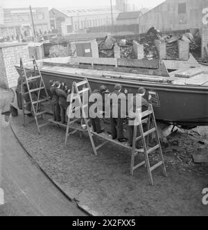 WRENS TRAINING FÜR NEUEN JOB: AUSBILDUNG FÜR SCHIFFSMECHANIKER DES ROYAL MARINEDIENSTES DER FRAUEN, ENGLAND, Großbritannien, 1943 - Frauen der WRNS stehen auf Planken, die auf Leitern ausgewuchtet sind, um im Rahmen ihrer Ausbildung Erkennungsbuchstaben auf die Seite eines Landungsfahrzeugs zu malen, wahrscheinlich im Slough Government Training Centre. Die Buchstaben wurden maßstabsgetreu in Kreide gezeichnet und werden mit einem Pinsel ausgefüllt. Nach der Erstellung wird diese Arbeit mit Schablonen ausgeführt, um Zeit zu sparen Stockfoto