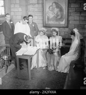 PFARRER: DAS WERK DES VIKARS DER ST. MARK'S CHURCH, VICTORIA DOCKS, SILVERTOWN, LONDON, ENGLAND, Großbritannien, 1944: Reverend Joseph Stephens leitet die Unterzeichnung des Registers nach einer Hochzeit in der St. Mark's Church in Silvertown. Es scheint eine „dreifache Hochzeit“ mit drei Bräuten und drei Bräutigamen gewesen zu sein! , Stockfoto