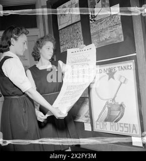 AUSSTELLUNG VON SPIELZEUG FÜR RUSSLAND, ST MARTIN's SCHOOL OF ART, LONDON, 1942 - Patricia Collins und Joan Hayes (15 Jahre) sind Monitore der Barnsbury County School in Woking. Hier sehen wir, wie sie eine Schriftrolle halten, auf der die Schule ihre Grüße an russische Kinder sendet. Der Gruß wurde in Form eines Sonetts verfasst. Hinter ihnen ist ein großes Brett mit Plakaten bedeckt, die von Kindern anderer Schulen gezeichnet wurden und die alle die Öffentlichkeit ermutigen, Russland zu unterstützen Stockfoto