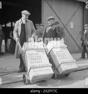 GROSSBRITANNIEN LIEFERT DIE WAREN IN KRIEGSZEITEN: HAFENARBEITER IN BRISTOL, ENGLAND, 1940 – Güterkisten werden aus einem Lagerhaus am Hafen in Bristol gerollt, bevor sie nach Kanada exportiert werden Stockfoto