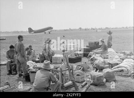 ROYAL AIR FORCE OPERATION IN FERNOST, 1941-1945 - umgeben von einer Sammlung von Gepäck, Zelten, Kisten und Hühnern, Personal einer RAF Spitfire Geschwader, die zu einem anderen Flugplatz in Zentralburma zieht, sehen Sie, wie eine Douglas Dakota Mark III der No. 117 Squadron RAF mit Ausrüstung für ihre neue britische Armee, Royal Flying Corps, Training Sqdn, 35, abhebt Stockfoto