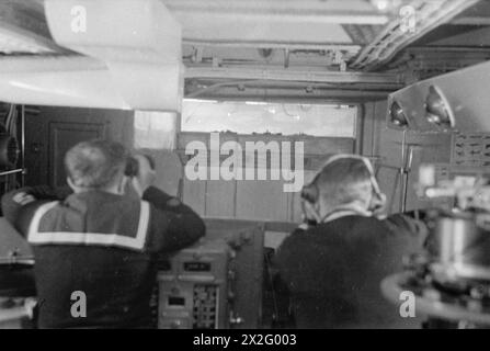 ENTWÄSSERUNG DES ROYAL NAVY-ZUGES AUF DEM MODERNEN SCHULSCHIFF. SEPTEMBER 1941 AN BORD DES ZERSTÖRER-DEPOT-SCHIFFES HMS TYNE. DIE DESTROYERMEN SIND AUSGEBILDET IN GESCHÜTZE, TORPEDOFEUER, U-BOOT-ABWEHR, SEEMANNSCHAFT UND SIGNALGEBUNG. ES WERDEN SCHIFFSMODELLE VERWENDET UND DIE BELEUCHTUNG IST SO ANGEORDNET, DASS SIE DIE EFFEKTE VON SCHEINWERFERN, STERNMUSCHELN UND GESCHÜTZBLITZEN ERZEUGT. - Ein Torpedoangriff, der von hinten auf der Brücke im Schützenraum gesehen wird Stockfoto