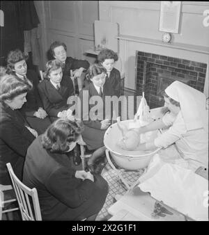 WRENS LERNEN MOTHERCRAFT: MITGLIEDER DES ROYAL MARINEDIENSTES DER FRAUEN ERHALTEN EINE AUSBILDUNG VON DER MOTHERCRAFT TRAINING SOCIETY, LONDON, ENGLAND, UK, 1945 - Eine Gruppe von Frauen der WRNS erhält eine Lektion im Baden eines Babys von Matron Miss Maslen-Jones von der Mothercraft Training Society, wahrscheinlich am MTS-Hauptsitz in Highgate, London. Die Originalunterschrift beschreibt die richtige Art, ein Baby zu baden, wie folgt: „Das Baby wird freigelegt und gründlich in die Falten geseift und dann direkt in die Badewanne gehoben. Seife wird nie im Gesicht Ihres Babys verwendet, und der Kopf wird immer über dem Ba gewaschen Stockfoto