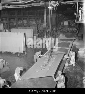 FABRIKWOHLFAHRT: WOHLFAHRT IN PILKINGTON'S GLASFABRIK, ST HELENS, LANCASHIRE, ENGLAND, VEREINIGTES KÖNIGREICH 1944: Arbeiten in einer Glasfabrik, wahrscheinlich in der Pilkington Glasfabrik in St. Helens. Eine große Glasplatte wird nach dem Gießen mit einem Kran auf die Schleifmaschine übertragen, die das Glas schleift und poliert. Die Arbeiter führen die große Glasplatte auf einen beweglichen Tisch, der das Glas unter den Schleif- und Polierwerkzeugen trägt Stockfoto