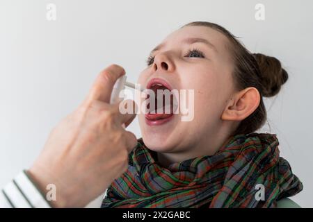 Ein krankes kleines Mädchen, dessen Mutter ihr Medizin in den Hals spritzt. Ausgewählter Fokus. Hochwertige Fotos Stockfoto