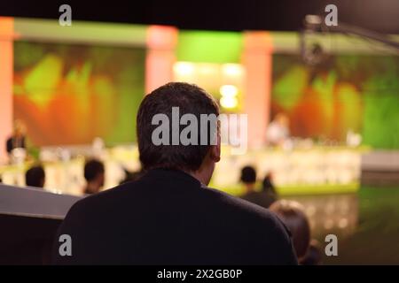 Der Mann sitzt im Fernsehstudio und sieht die Show auf der Bühne, dahinter Stockfoto