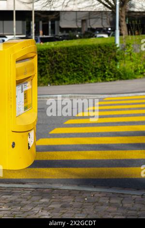 Zürich, Schweiz - 2. April 2024: Öffentlicher gelber Strassenbriefkasten in Kombination mit gelbem Zebra in der Schweiz Stockfoto