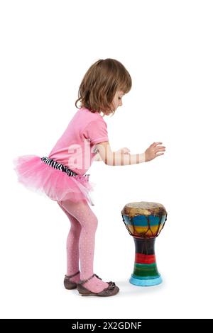 Kleines Mädchen in Pink, das auf dem Djembe spielt und ihre Zunge aus dem Eifer rauszieht. Stockfoto