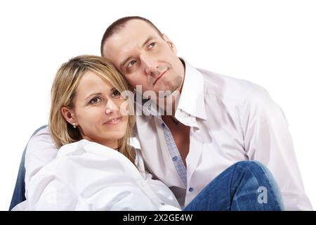 Nahaufnahme junge Frau und Mann in weißen Hemden und blauen Jeans sitzen auf dem Boden und sehen leicht lächelnd in eine Richtung aus. Stockfoto