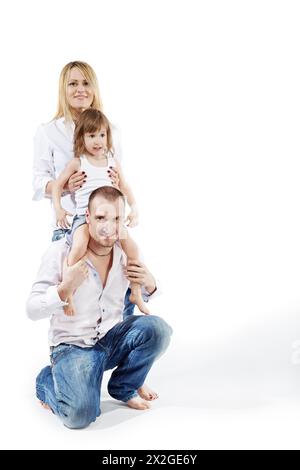 Vater steht auf einem Knie, kleine Tochter sitzt auf seinen Schultern und Mutter stützt sie von hinten. Stockfoto