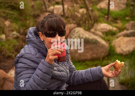 Lateinische Frau, Rucksackreisender, frühstückt auf einem Campingplatz, freut sich, einen neuen Tag ihres Outdoor-Urlaubs zu beginnen. Stockfoto