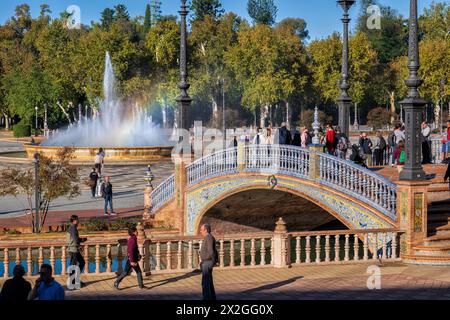 Sevilla, Spanien - 24. Oktober 2023: Menschen an der Plaza de Espana mit Brücke über Kanal und Brunnen im Maria-Luisa-Park, Wahrzeichen der Stadt. Stockfoto