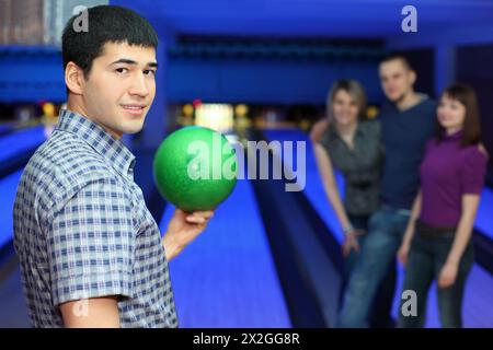 Ein Mann steht seitwärts und hält Ball für Bowling und drei Freunde hören ihn, konzentrieren sich auf den Mann Stockfoto