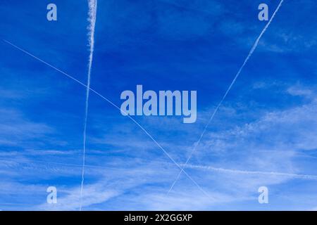 Überqueren Sie weiße Dampfpfade (Kondensstreifen) vor dem blauen Himmel, Surrey im Frühjahr, von Flugzeugen, die zum und vom Flughafen London Heathrow fliegen Stockfoto