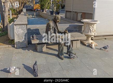 Craiova, Rumänien - 16. März 2024: Bronzestatue des Menschen, der Tauben füttert, sitzt auf der Bank von König Ferdinand und dem Platz der Königin Maria im Stadtzentrum von Sp Stockfoto