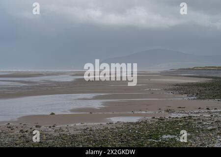 Breiter, weitläufiger Strand am Westufer, Walney Island, Barrow-in-Furness, Cumbria, unter grauem stürmischem Himmel mit Black Combe Mountain im Hintergrund. Stockfoto