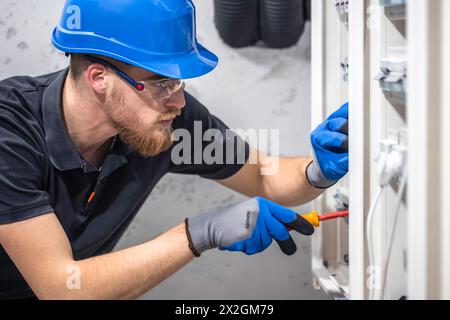 Ein Elektriker arbeitet in einer Schalttafel mit einem elektrischen Anschlusskabel. Stockfoto