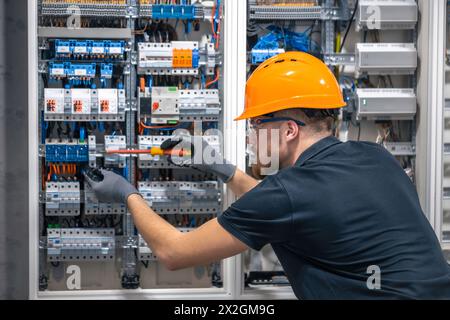 Ein Elektriker arbeitet in einer Schalttafel mit einem elektrischen Anschlusskabel. Stockfoto