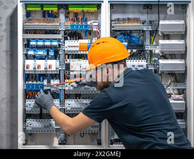 Ein Elektriker arbeitet in einer Schalttafel mit einem elektrischen Anschlusskabel. Stockfoto