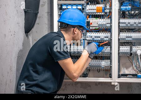 Ein Elektriker arbeitet in einer Schalttafel mit einem elektrischen Anschlusskabel. Stockfoto