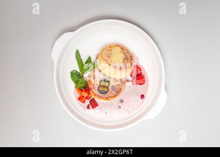 Runde, flauschige Hüttenkäse-Pfannkuchen mit lebendigen Erdbeeren und Heidelbeeren auf einem weißen Teller, perfekt für ein köstliches Frühstück. Stockfoto