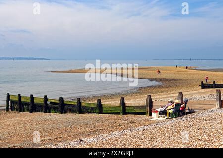 Menschen, die sich in der Frühlingssonne neben Wellenbrechern am Hill Head Beach, Lee-on-the-Solent, Fareham Hampshire, ausruhen Stockfoto