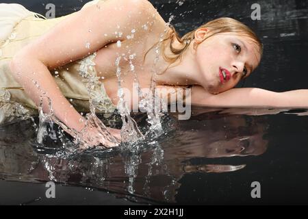 Das hübsche, nachdenkliche Mädchen im Kleid mit Korsett liegt auf nassem Boden und sprüht Wasser Stockfoto